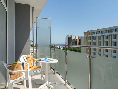 Balkon mit zwei Stühlen, Tisch und Blick auf benachbarte Gebäude bei klarem Himmel.