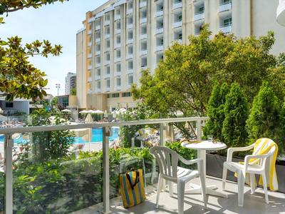 Blick von einem Balkon mit Stühlen und Tisch auf einen Pool vor einem mehrstöckigen Hotelgebäude.