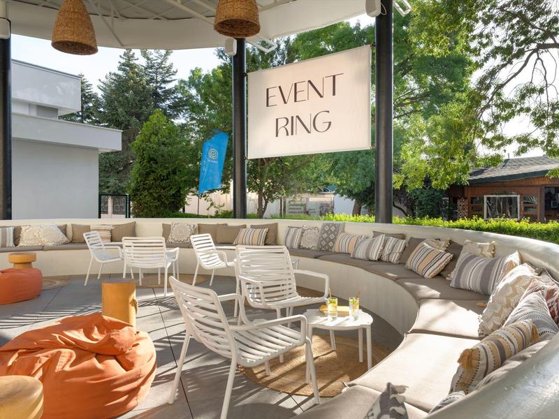 Gemütliche, runde Außensitzecke mit Kissen und Stühlen neben einem Event-Banner.