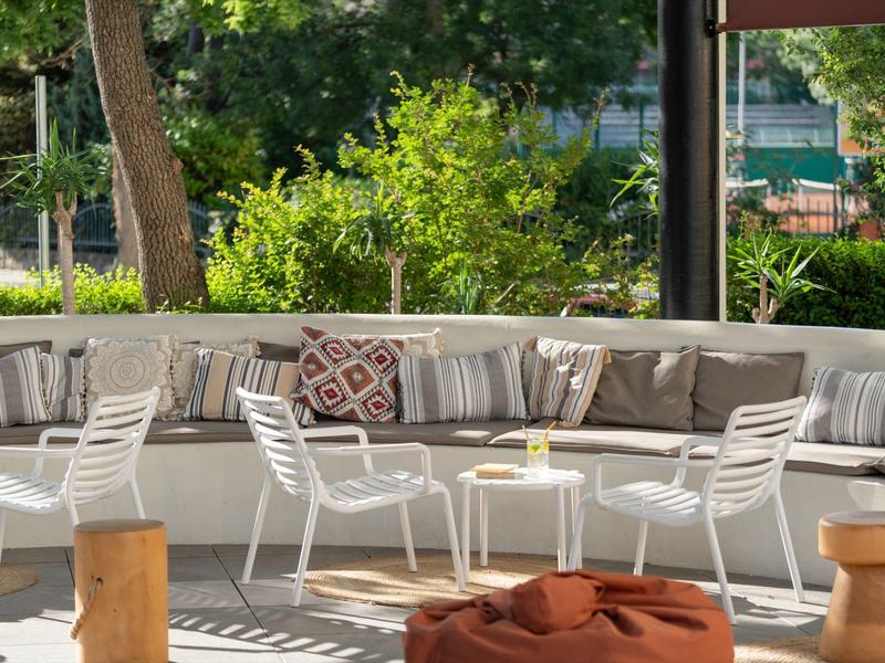 Gemütliche Outdoor-Lounge mit weißen Stühlen und großer halbkreisförmiger Couch bei Tageslicht.