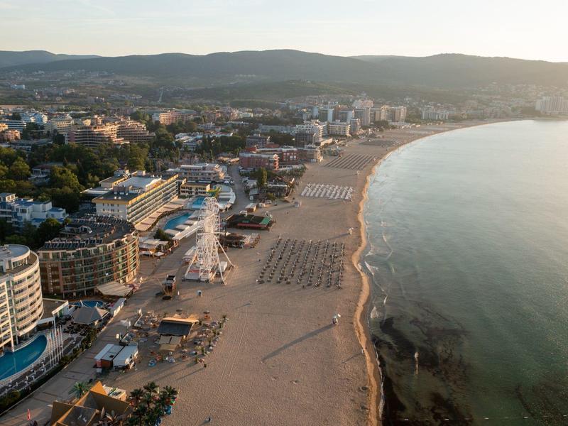 Luftaufnahme eines breiten Sandstrands mit Hotels und Stadt im Hintergrund bei Abendlicht