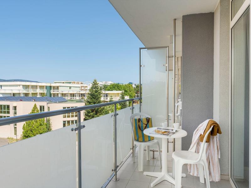 Balkon mit weißem Tisch und Stühlen, modernem Geländer und Blick auf benachbarte Gebäude.