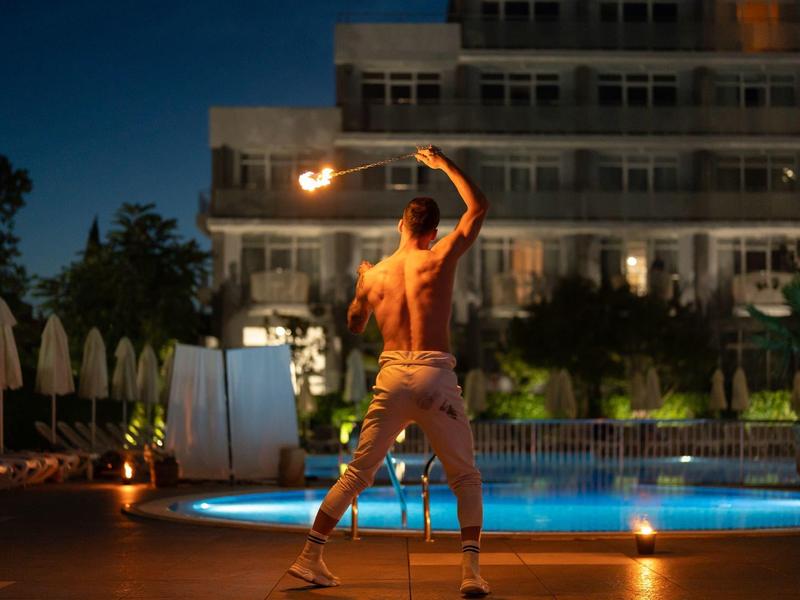 Ein Mann führt abends eine Feuershow neben einem beleuchteten Pool vor einem Hotel auf.