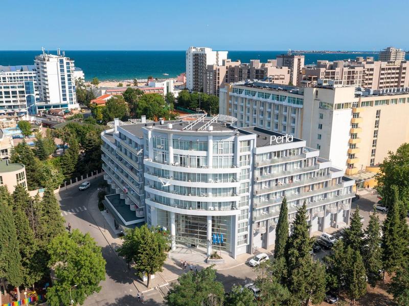 Modernes Hotelgebäude in Küstennähe mit umliegenden Bäumen und anderen Gebäuden.