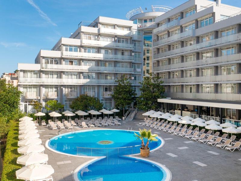 Modernes Hotel mit mehreren Etagen und zwei runden Außenpools, umgeben von Liegestühlen und Sonnenschirmen.