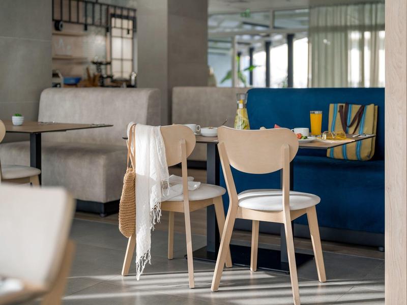 Heller, moderner Frühstücksraum mit Holzstühlen, weißen Kissen und grauen Sitzbänken.