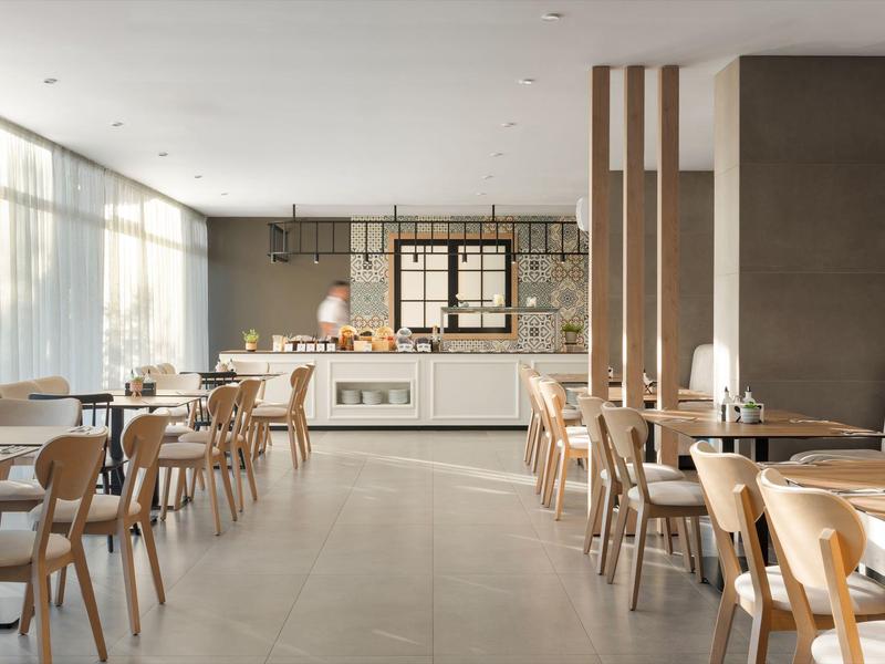 Helles, modernes Restaurant mit Holzstühlen, weißen Tischen und einem Buffetausgabebereich.