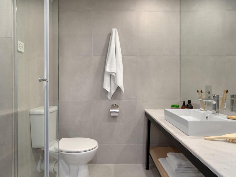 Modernes Badezimmer mit Toilette, Waschbecken auf einer langen Arbeitsplatte und Handtüchern.