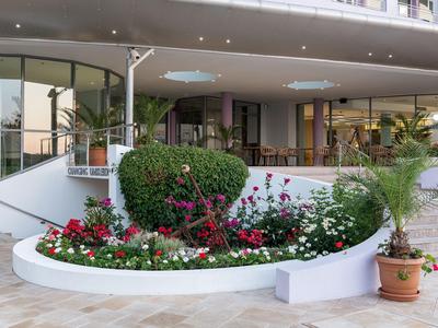 Elegante terrazza dell'hotel con aiuola, cespugli e vasi davanti a una facciata di vetro.