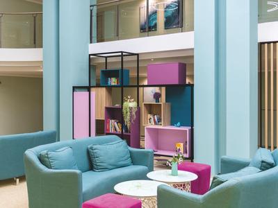 Modernes Wohnzimmer mit blauen Sesseln, pinken Poufs und buntem Regal als Raumteiler.