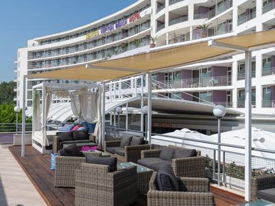 Große Terrasse mit modernen Rattanmöbeln, Sitzkissen und Sonnensegeln an weißem Wohngebäude.