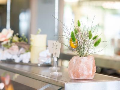 Grüne Zweige in rosa rosa Salzstein-Vase auf glänzendem Metalltisch in heller Raumumgebung.