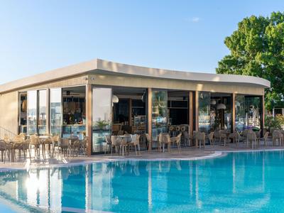 Modernes Hotelrestaurant mit Glasfront und Außenbereich am großen Pool bei sonnigem Wetter.