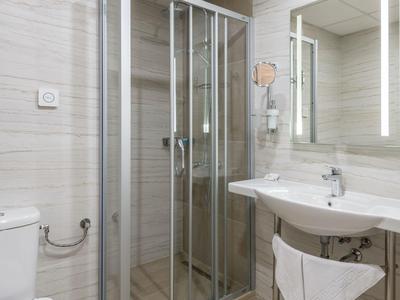 Modernes Hotelbadezimmer mit Dusche, Waschbecken, Spiegel und WC in neutralen Farben.