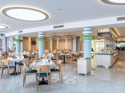 Moderner Hotelrestaurantbereich mit runden Tischen, Stühlen und hellen Deckenleuchten.