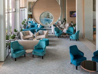 Moderner Wartebereich mit blauen Sesseln, großen Fenstern und runden Spiegeln an der Wand.