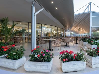 Offener Hotelterrassenbereich mit Tischen, Stühlen und Blumenkästen unter modernem Dach.
