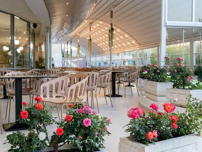 Moderner Außenbereich eines Hotels mit weißen Tischen und Stühlen, umgeben von bunten Blumen.