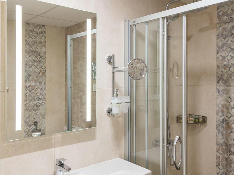 Moderner Badezimmerbereich mit Glas-Dusche, großem Spiegel und weißem Waschbecken.