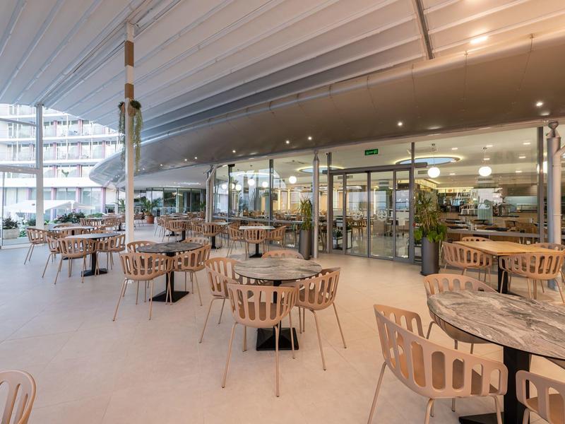 Moderne Außenterrasse eines Hotels mit Holzstühlen und Marmor-Tischen unter einem großen Sonnendach.