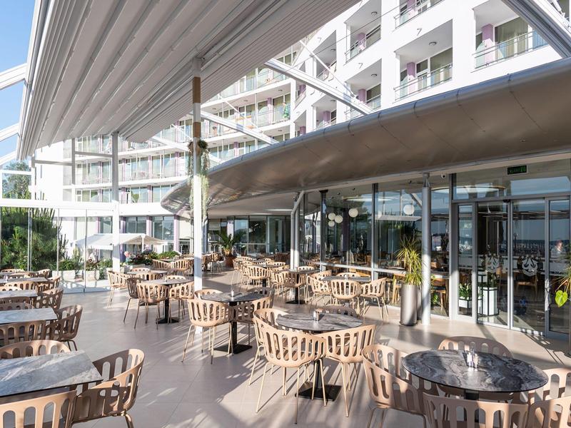 Große Hotelterrasse mit vielen Tischen und Stühlen unter Sonnenschutz.