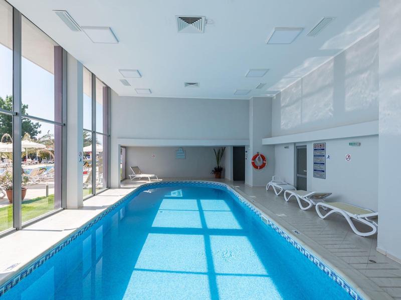 Innenpool mit Sonnenlicht und Liegestühlen neben großen Fenstern mit Blick auf den Garten.