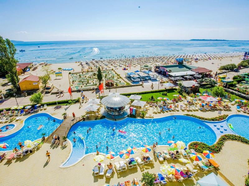 Großer Poolbereich mit Liegestühlen am Strand und Blick auf das Meer bei klarem Himmel.