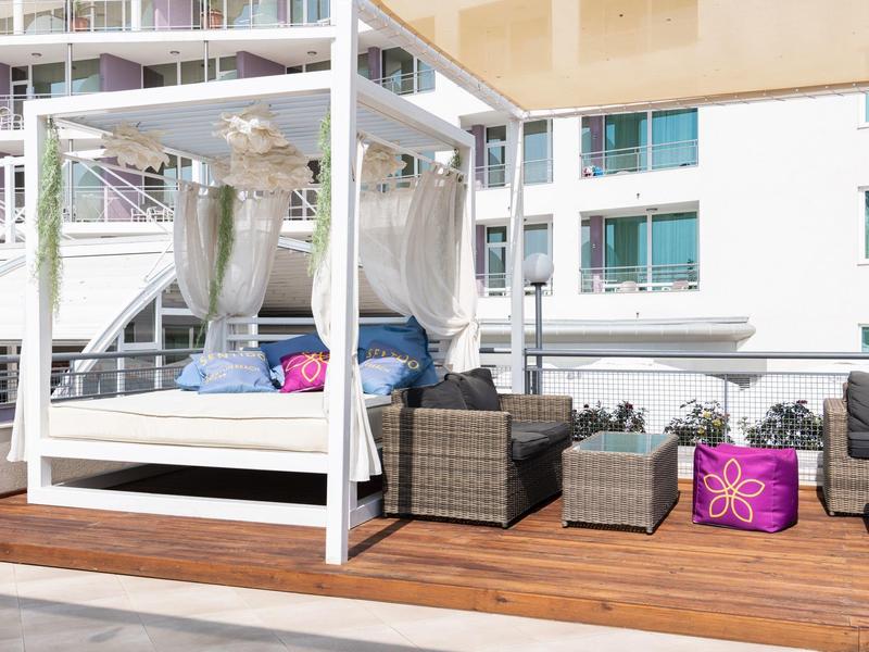 Moderner Außenbereich mit weißem Himmelbett, grauen Polstermöbeln und Holzboden auf Balkon.