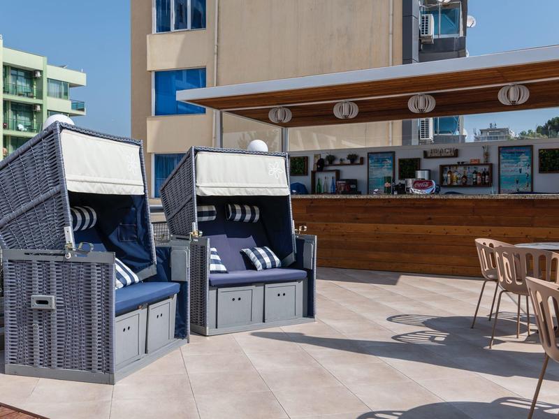 Zwei Strandkörbe vor einer modernen Bar mit Holzmöbeln auf einer sonnigen Terrasse.