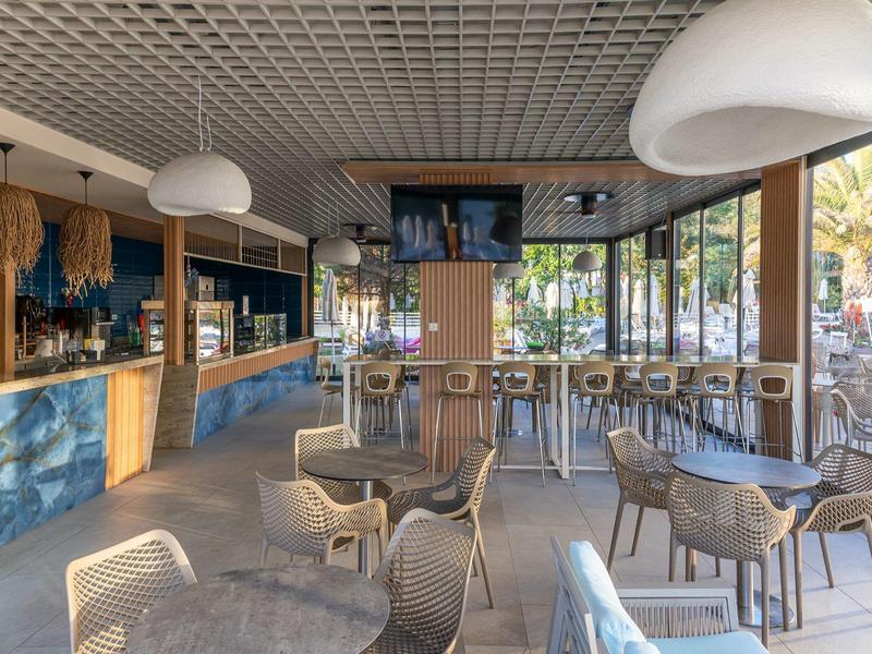 Helles, modernes Café mit vielen Stühlen und großen Fenstern, Blick auf Außenbereich.