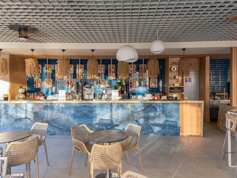 Moderner Hotelbarbereich mit blau beleuchtetem Tresen, Stühlen und Tischen in hellem Raum.