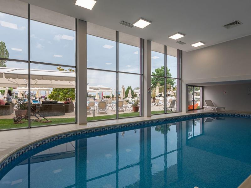 Innen-Schwimmbad mit großen Glasfenstern und Blick auf Liegestühle und Garten draußen.