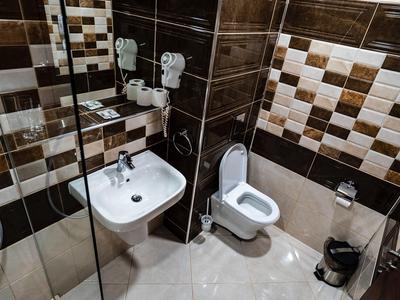 Kompaktes, modernes Hotelbad mit Toilette, Waschbecken, Glas-Duschwand, braunen Fliesen und Spiegel.