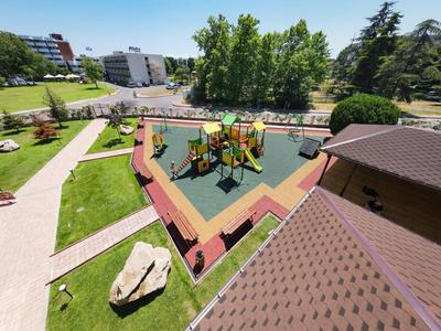 Bunter Kinderspielplatz mit Klettergeräten auf weichem Boden neben Grünflächen und Gebäuden.