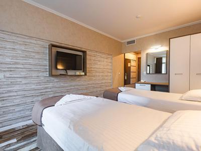 Modern eingerichtetes Hotelzimmer mit zwei Einzelbetten, Flachbildfernseher und hellem Interieur.