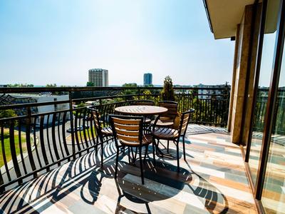 Balkon mit runden Tisch und Stühlen, Blick auf Stadt und Himmel bei Tageslicht.