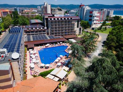 Hotelkomplex mit großem Pool, Sonnenschirmen und umliegenden modernen Gebäuden in einer Stadtlandschaft.