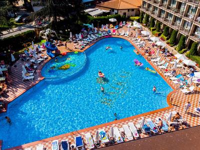 Großer Hotelpool mit Liegestühlen und Gästen bei sonnigem Wetter.