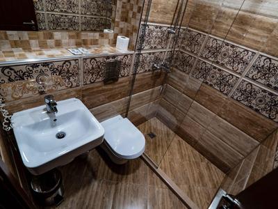 Kleines Bad mit Eckdusche, weißem Waschbecken und Toilette in braun gefliesten Wänden.