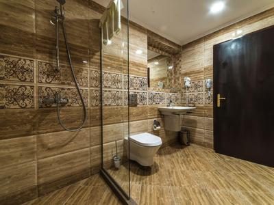 Modernes Badezimmer mit beiger Fliesenwand, Toilette, Waschbecken und Glastür zur Dusche.