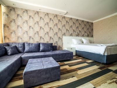 Modern eingerichtetes Hotelzimmer mit grauem Sofa, Bett und gemustertem Holzboden.
