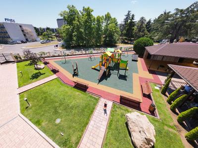 Moderner, bunter Spielplatz mit Klettergerüst und Rutschen neben einem Hotelgebäude und Garten.