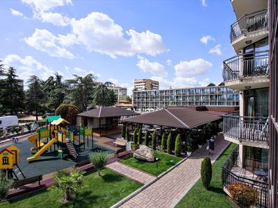 Ein Hotel mit Außenpool, Spielplatz und grünen Bereichen unter blauem Himmel.