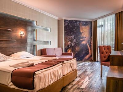 Modernes Hotelzimmer mit Doppelbett, Holzboden und großem Wandbild neben Fenstern mit Vorhängen.