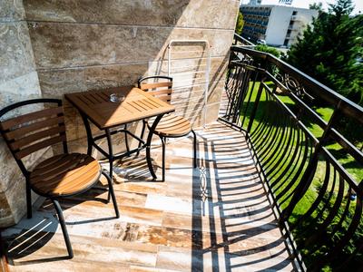 Balkon mit zwei Stühlen, Tisch und Steinwand, Sonnenschein wirft Schatten auf Bodenfliesen.