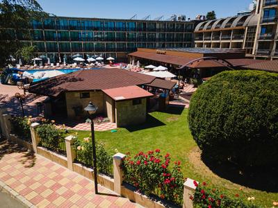 Hotel mit Pool, Liegestühlen, Sonnenschirmen und gepflegtem Garten bei Sonnenschein.