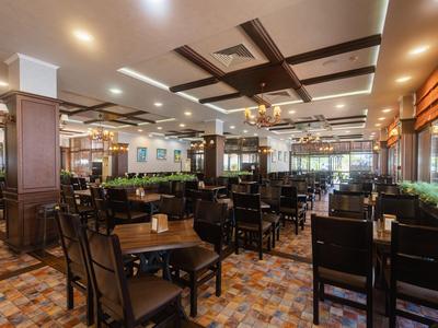 Großer Hotelrestaurantbereich mit Holzstühlen, Tischen und dekorativem Deckenstrukturelement.