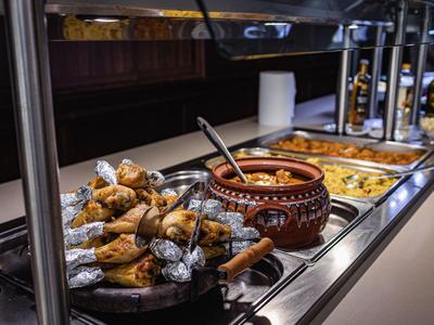 Buffet mit gebratenem Hähnchen, einer Schüssel Sauce und weiteren warmen Speisen in einer Hotelküche.