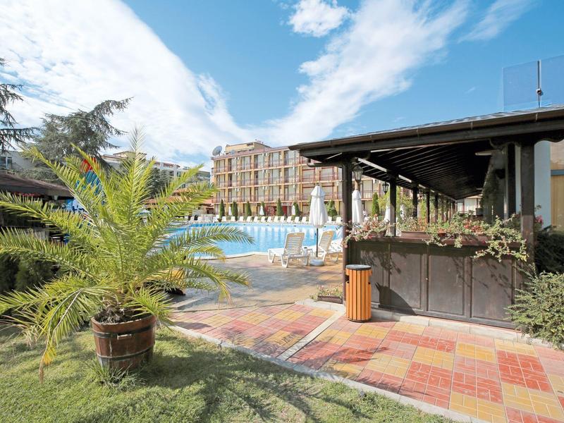 Hotel met groot zwembad, parasols en palmbomen onder een blauwe lucht.