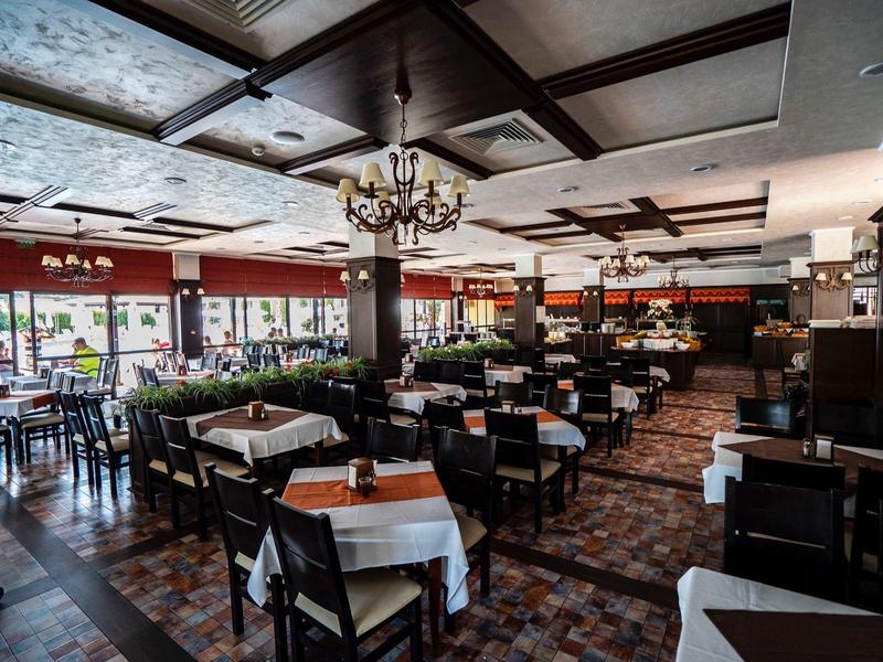 Elegant restaurant met houten meubilair, witte tafelkleden, kroonluchters en veel natuurlijk licht.